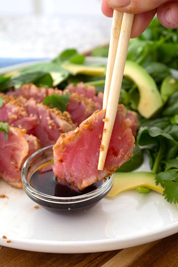 holding piece of seared ahi tuna being dipped in soy sauce with chopsticks
