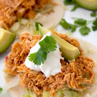 tortilla with shredded lettuce, taco meat, sour cream, avocado and cilantro garnish on a white platter