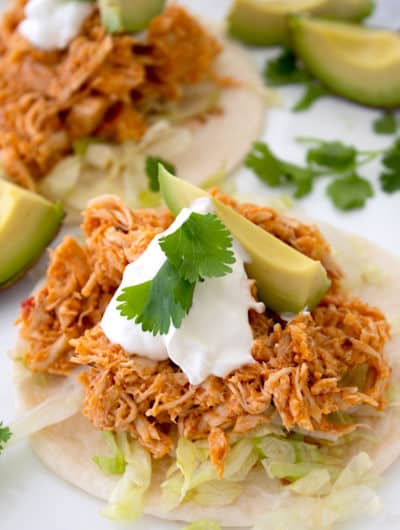 tortilla with shredded lettuce, taco meat, sour cream, avocado and cilantro garnish on a white platter