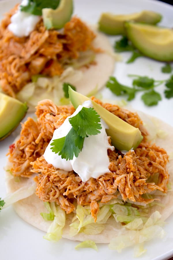 tortilla with shredded lettuce, taco meat, sour cream, avocado and cilantro garnish on a white platter