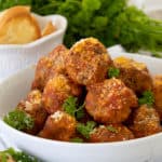 meatballs on a white bowl platter with parsley and crostini in background