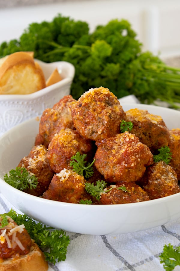 meatballs on a white bowl platter with parsley and crostini in background 