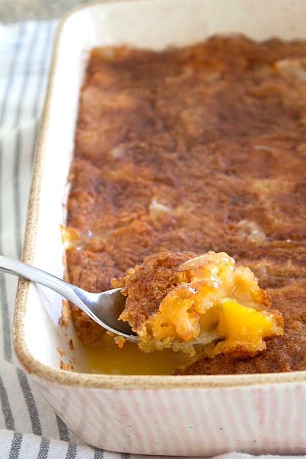 peach dump cake in a casserole dish being spooned