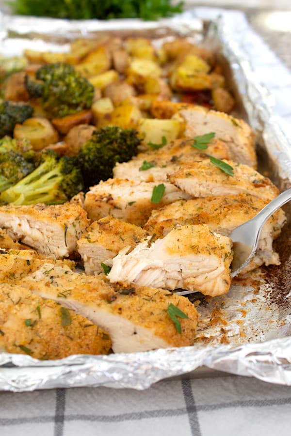 sheet pan full of chicken on a fork with broccoli and potatoes
