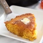 white plate with slice of skillet cornbread with honey and butter on top