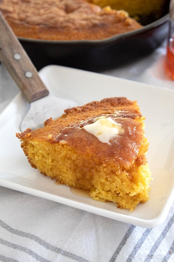 white plate with slice of skillet cornbread with honey and butter on top