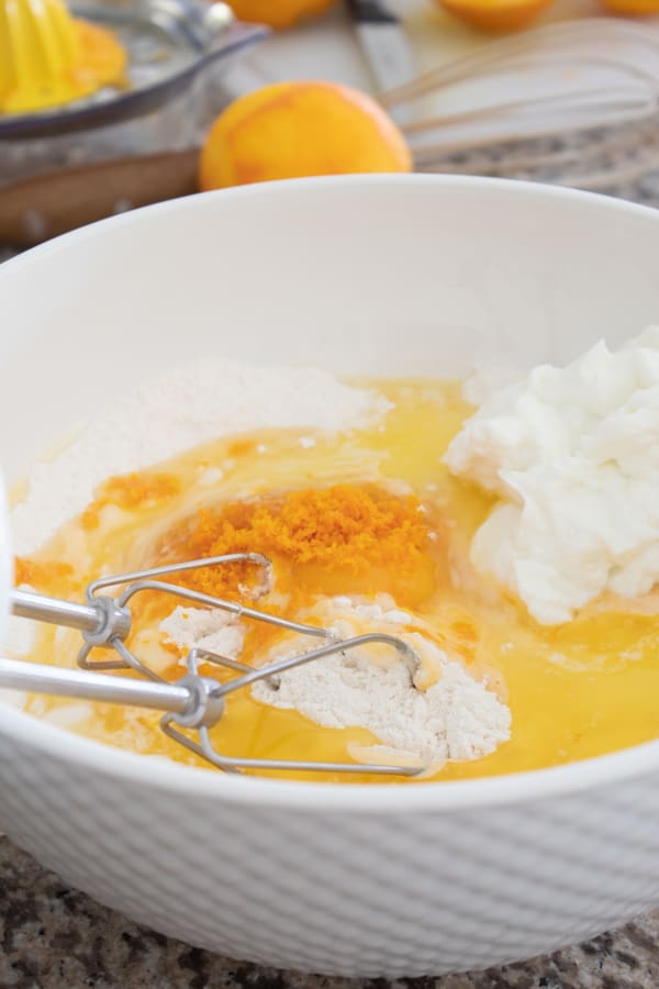 mixing batter for orange muffin in a white ceramic mixing bowl