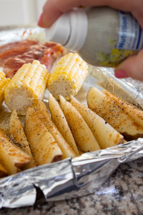 potatoes chicken and corn being sprayed with nonstick spray 