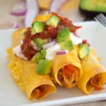 baked chicken taquitos with sour cream avocado and salsa on a white plate