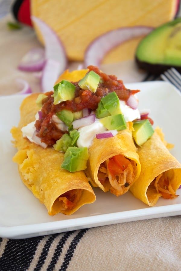 baked chicken taquitos with sour cream avocado and salsa on a white plate