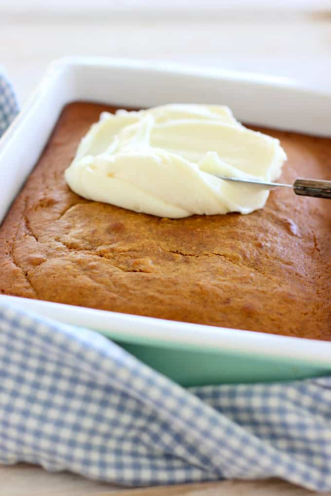 baked pumpkin cake with cream cheese frosting being spread