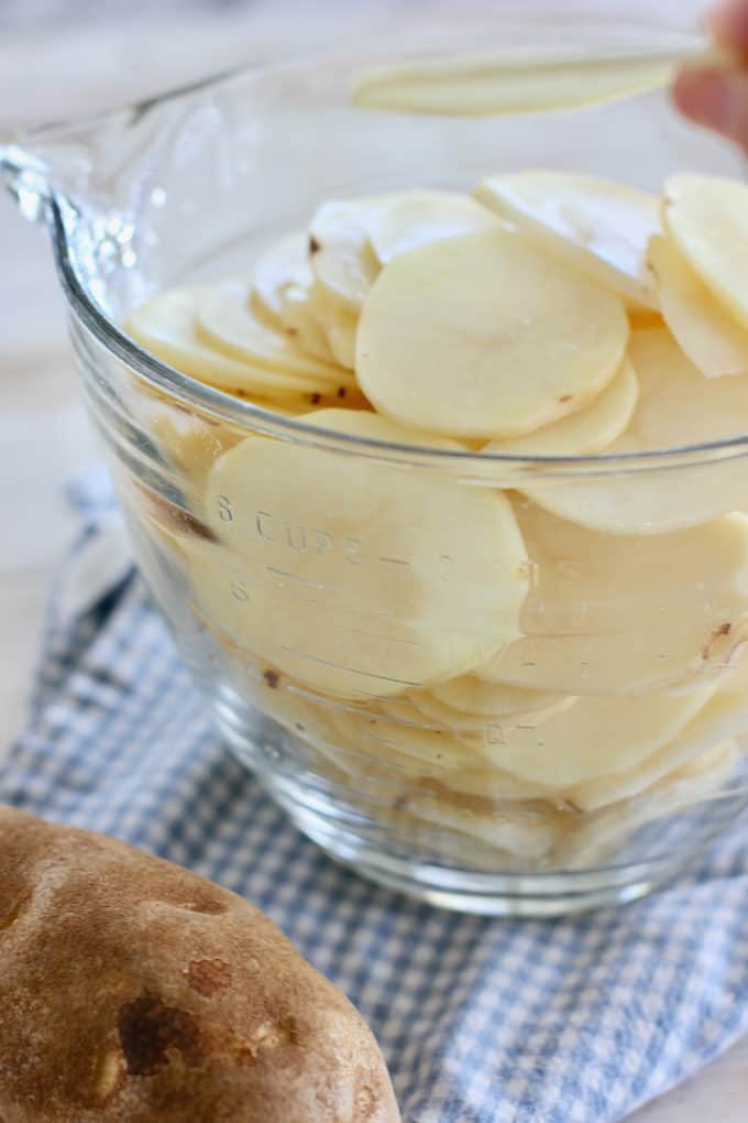 thinly sliced potatoes in a large white measuring cup