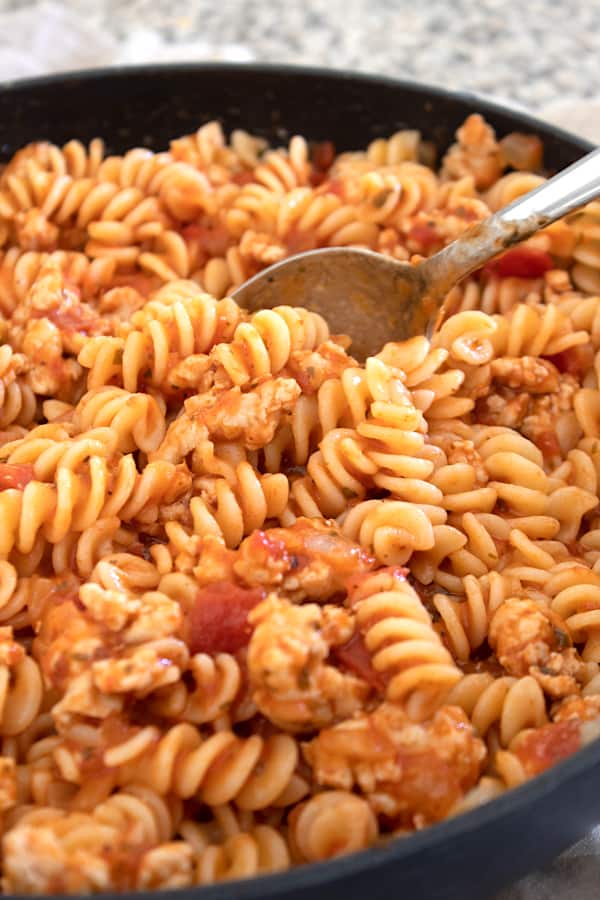 stirring ground chicken and pasta in a skillet