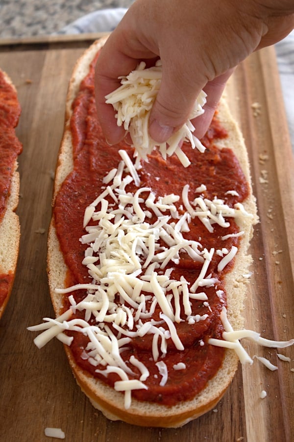 adding pizza sauce and mozzarella to a French loaf
