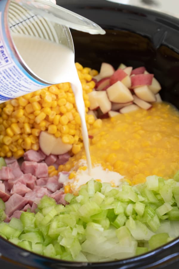 pouring evaporated milk into chowder in slow cooker