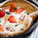 dutch baby in pan with whipped cream and berries