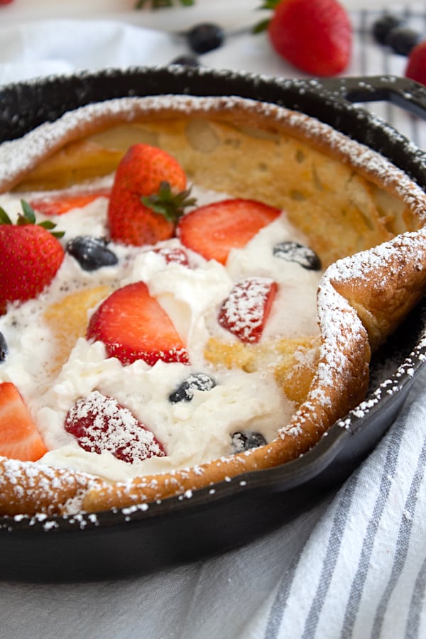 dutch baby in pan with whipped cream and berries