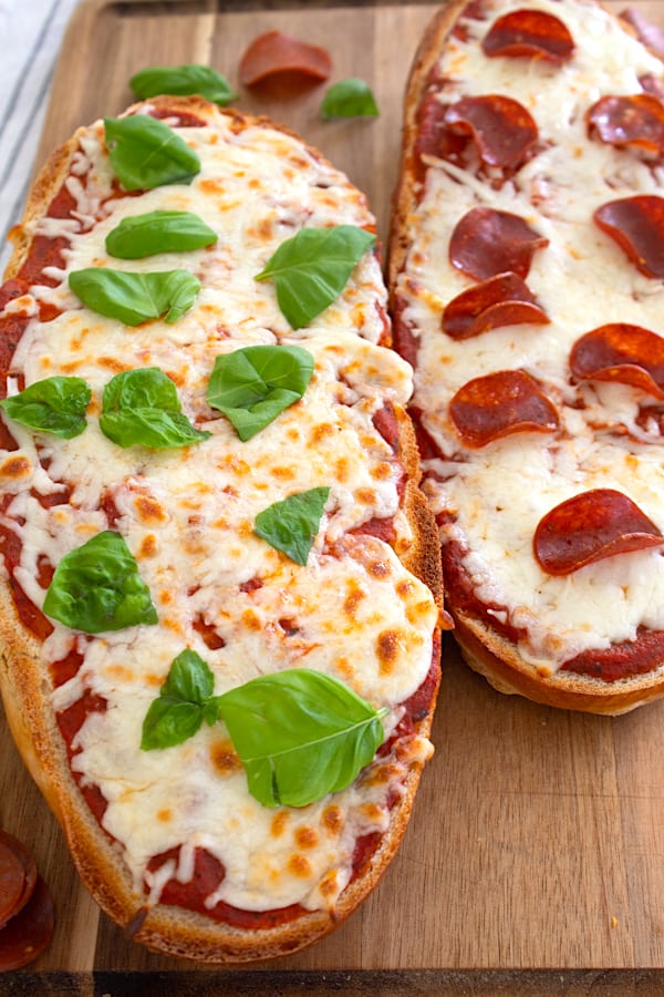 side by side French bread pizzas with different toppings of basil and pepperoni