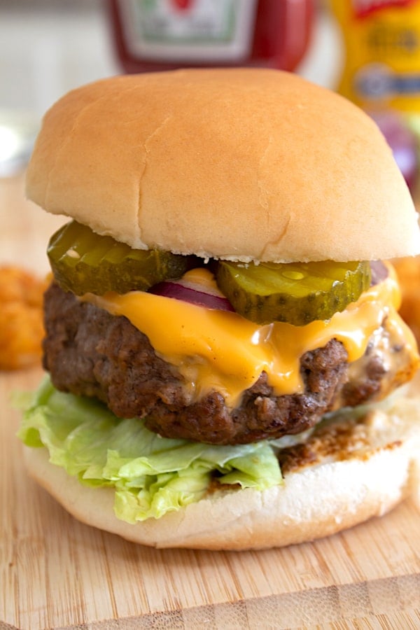 front view of a cheeseburger with condiments in the background