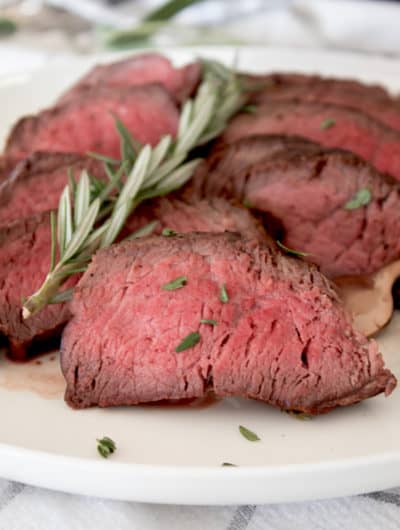 seared medium steak on a white plate with rosemary garnish