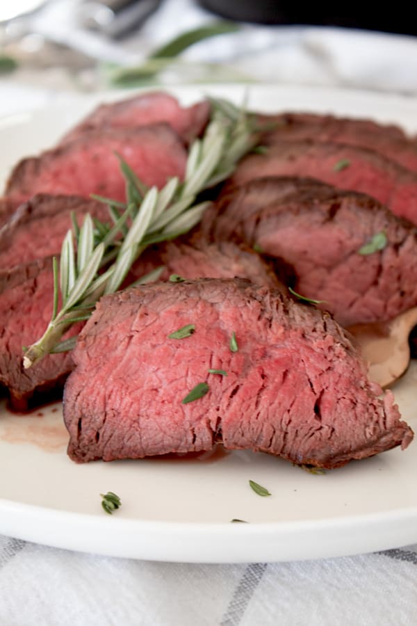 seared medium steak on a white plate with rosemary garnish