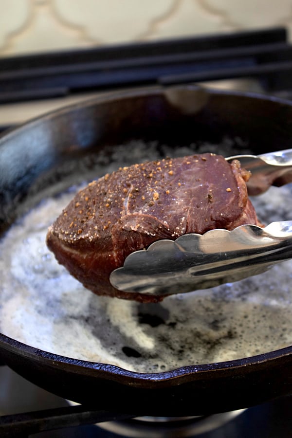adding baked steak to cast iron pan to sear
