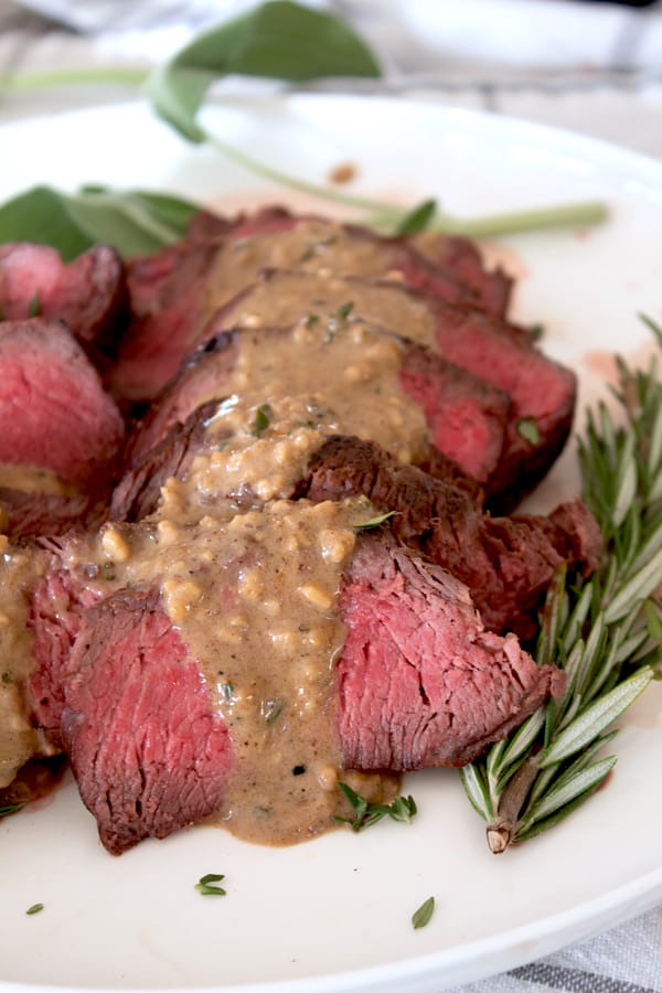 sliced steak with pan sauce and rosemary garnish sprig