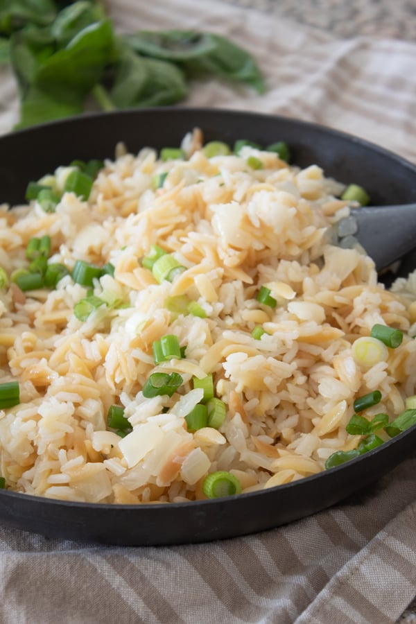 black pan full of cooked rice pilaf garnished with green onion
