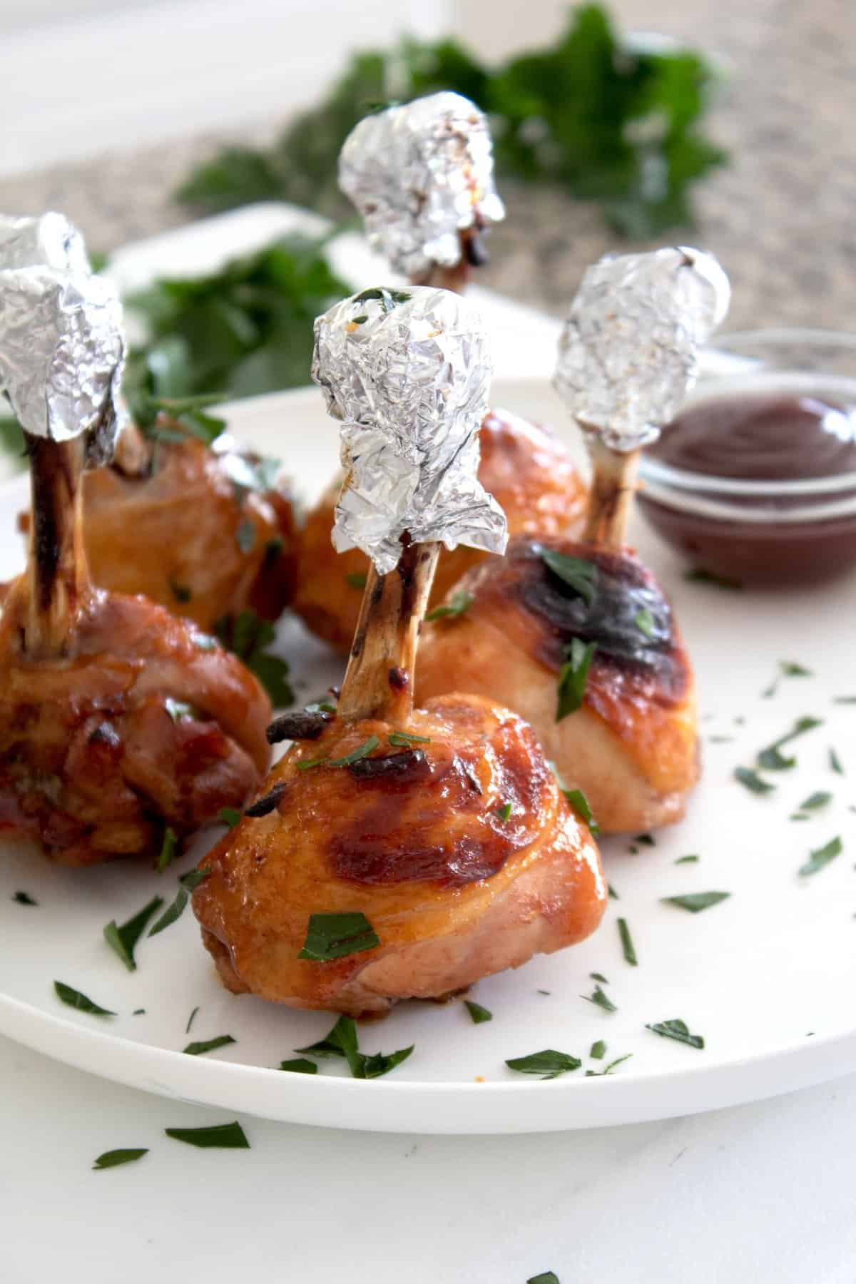 chicken lollipops on a white plate garnished with parsley flakes