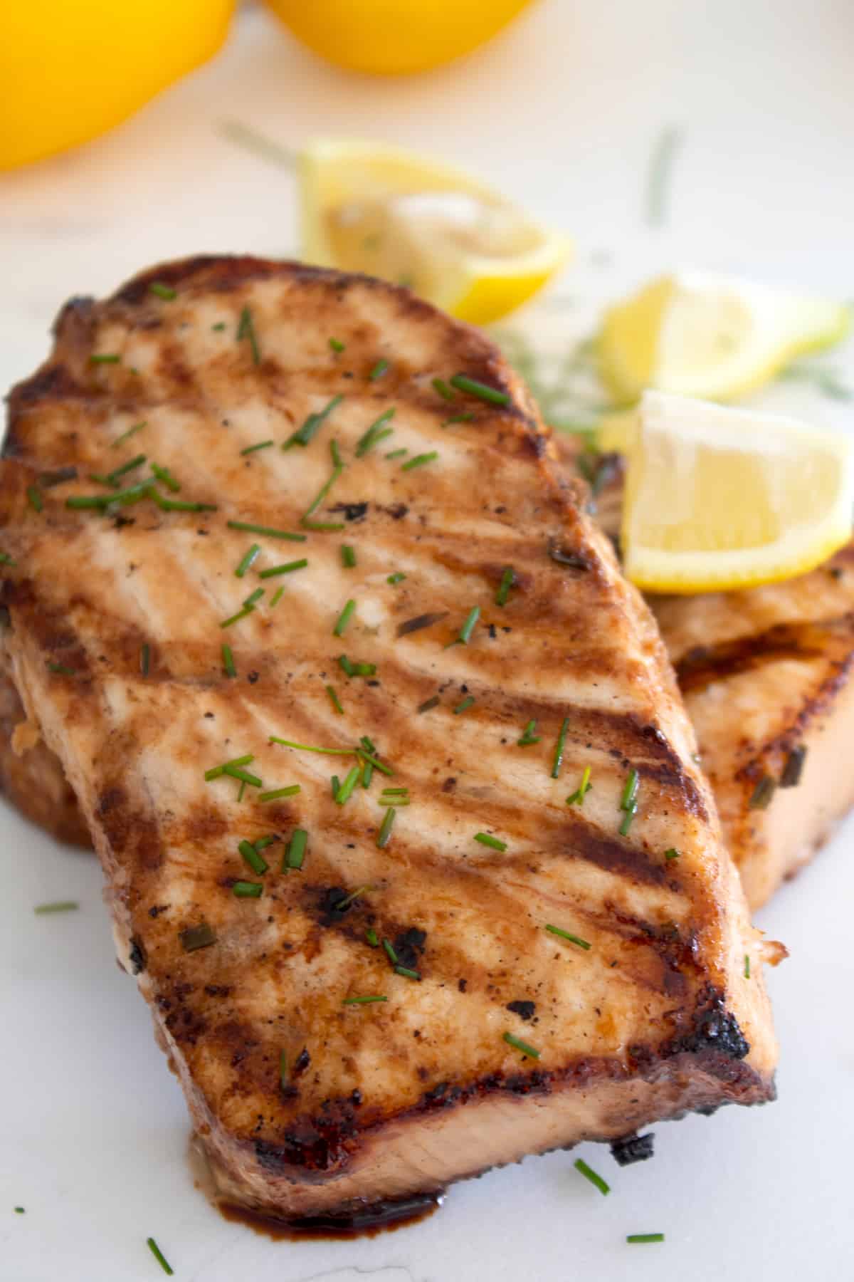closeup of grilled swordfish on a white plater garnished with lemons