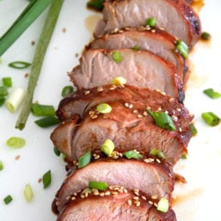 sliced pork tenderloin on a plate garnished with green onion