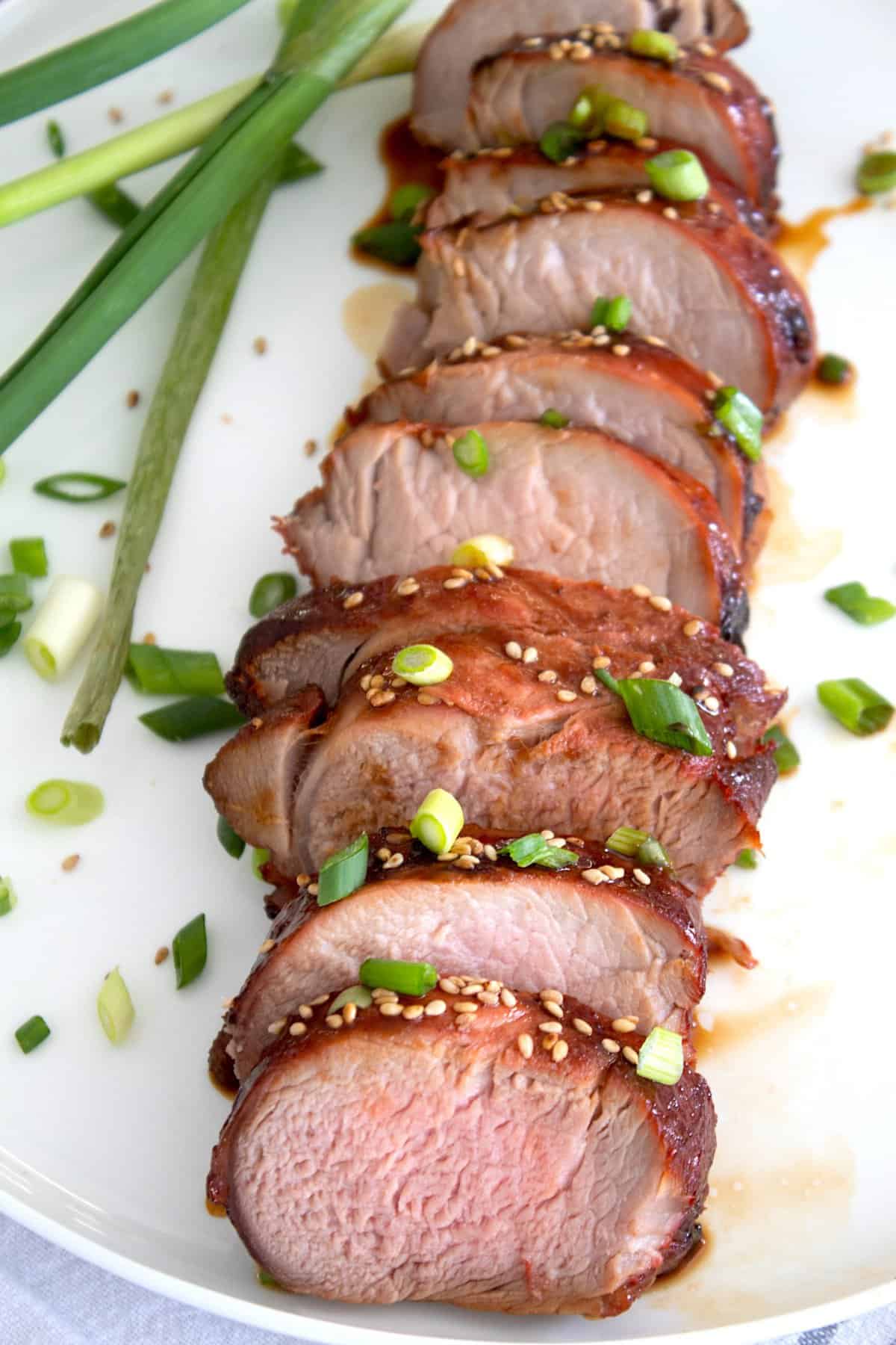 sliced pork tenderloin on a plate garnished with green onion
