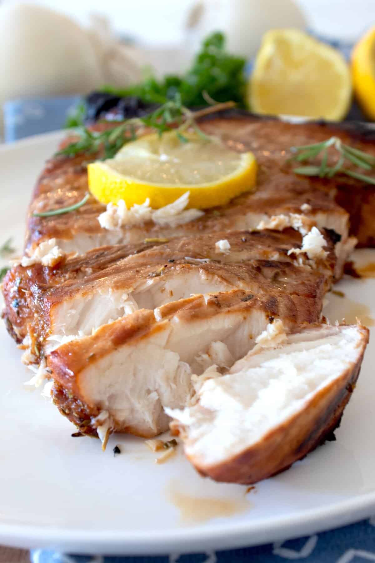 cut and sliced marinated swordfish with lemon and rosemary garnish