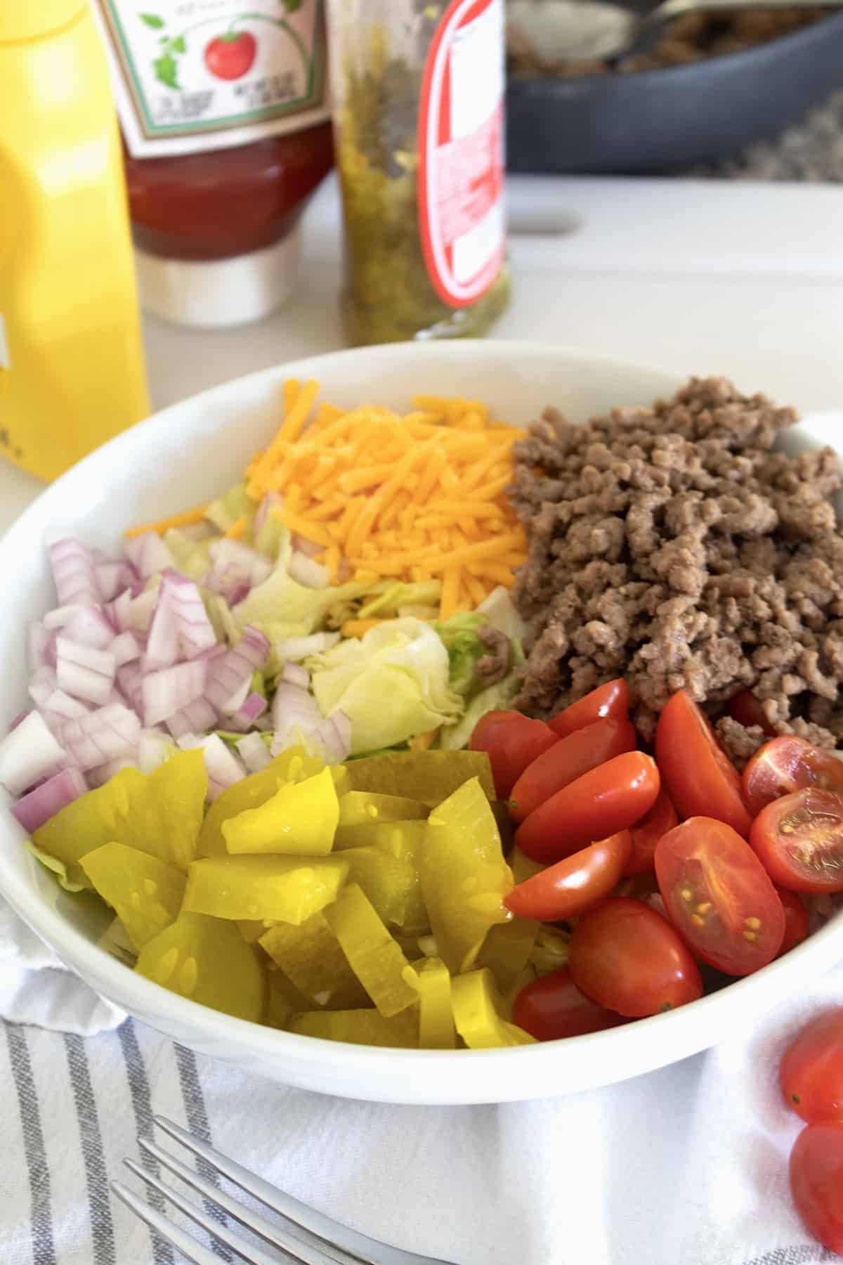 cheeseburger salad layered with ingredients in a white bowl