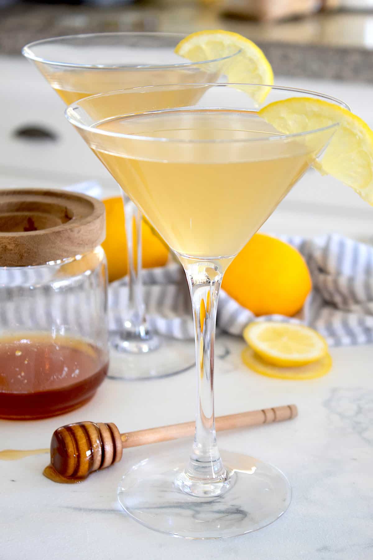 bees knees cocktail in martini glasses with lemon garnish and honey swizzle in foreground