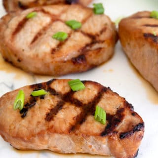 grilled pork chop served on a white cutting board garnished with green onion