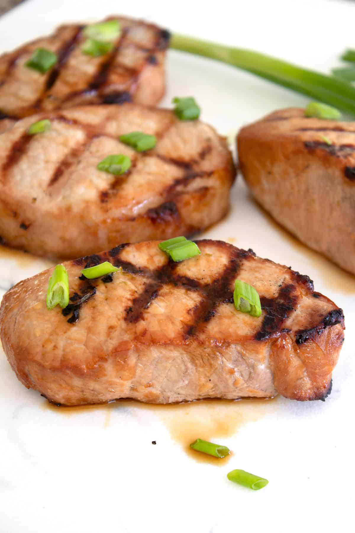 grilled pork chop garnished with green onions on white cutting board