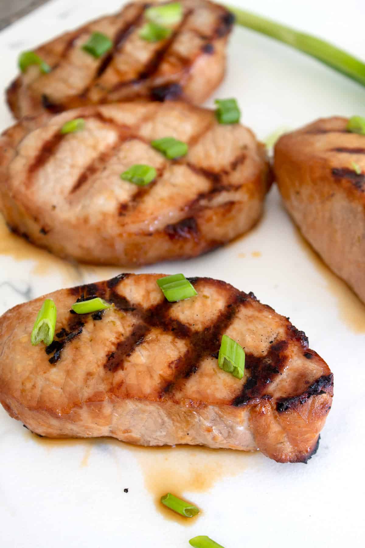 grilled pork chop served on a white cutting board garnished with green onion