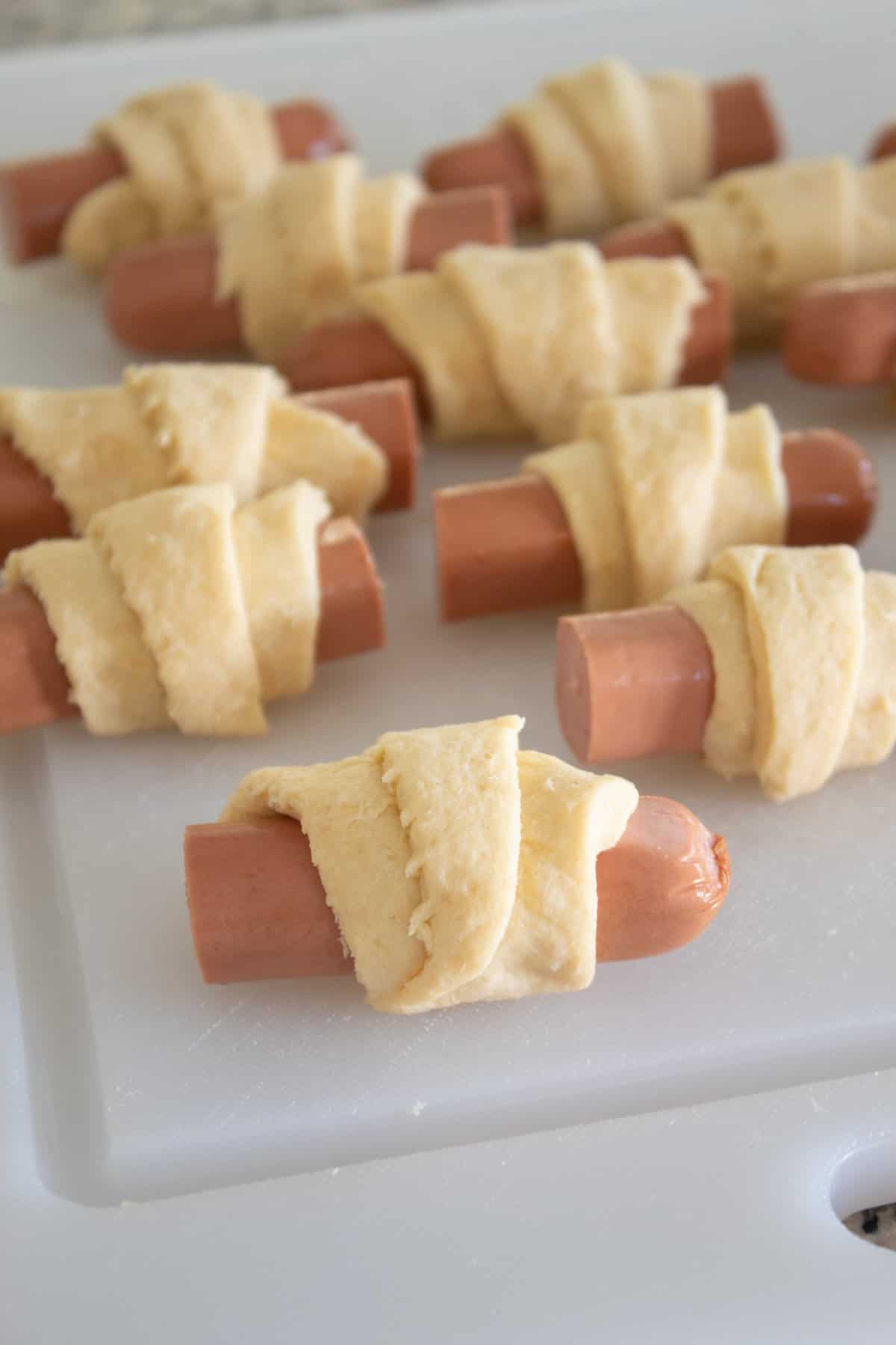 raw pigs in a blanket on a cutting board before baking