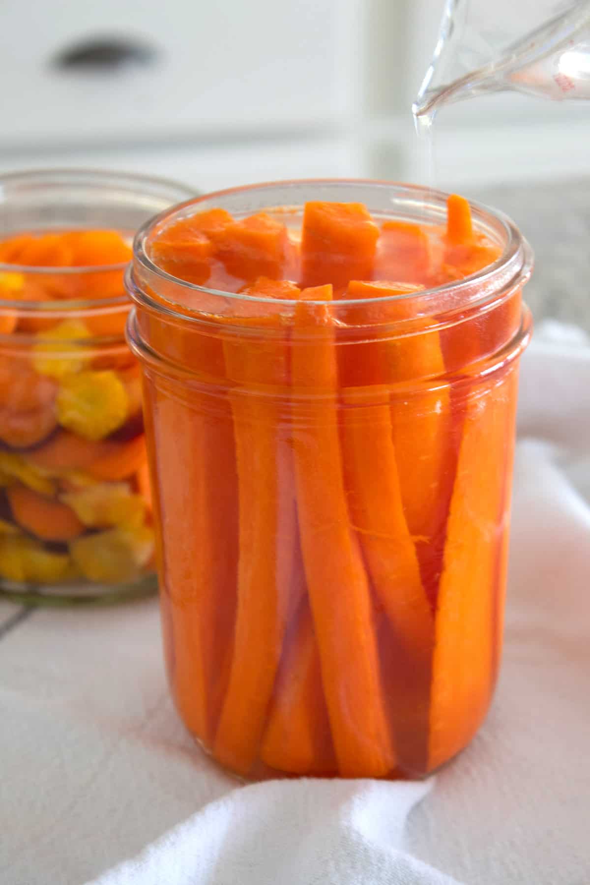 pouring brine over carrots in a jar