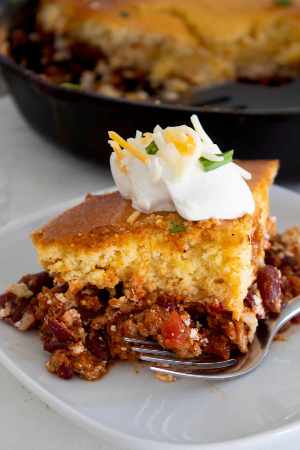 chili cornbread casserole on a white plate topped with sour cream chives and cheddar cheese