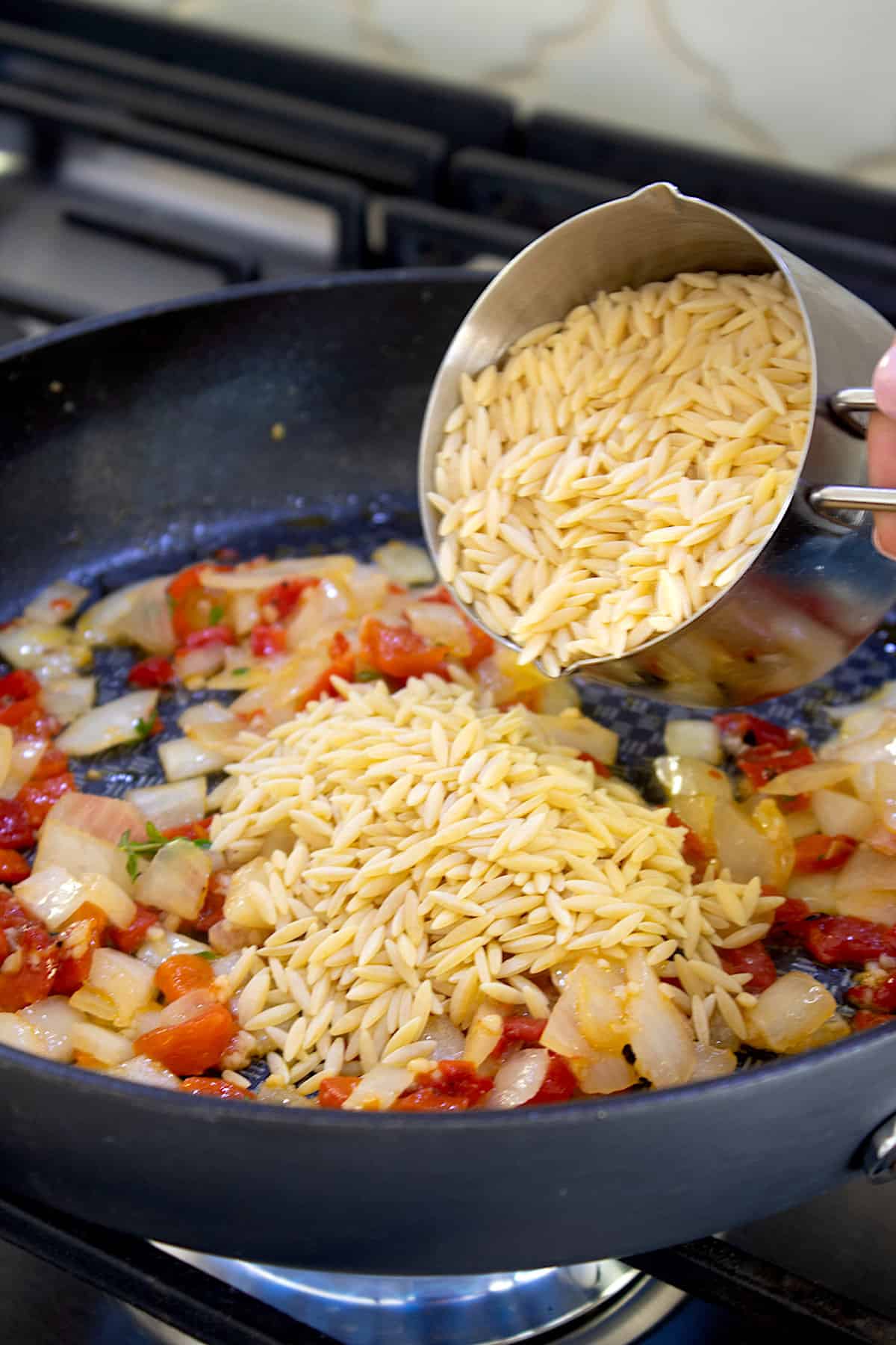 sautéing peppers onions and orzo in a pan