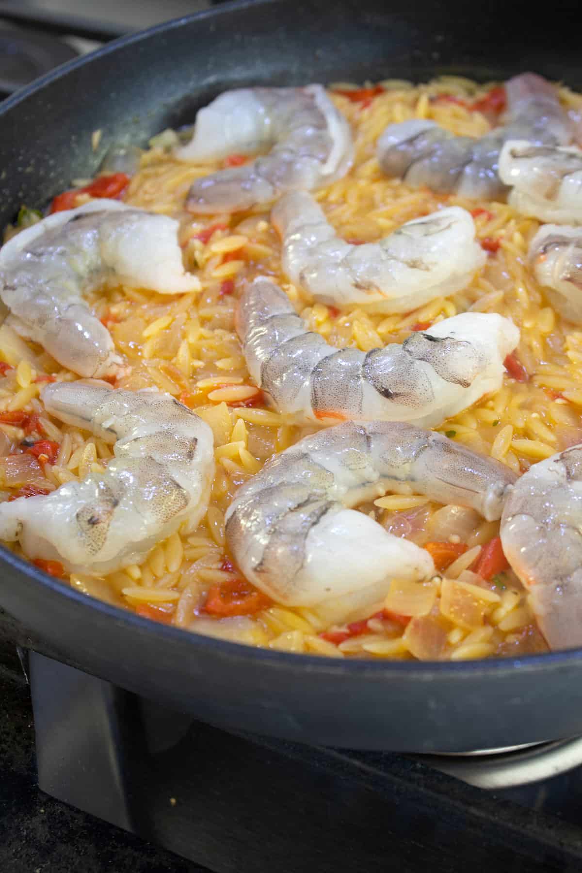 adding shrimp on top of orzo to cook