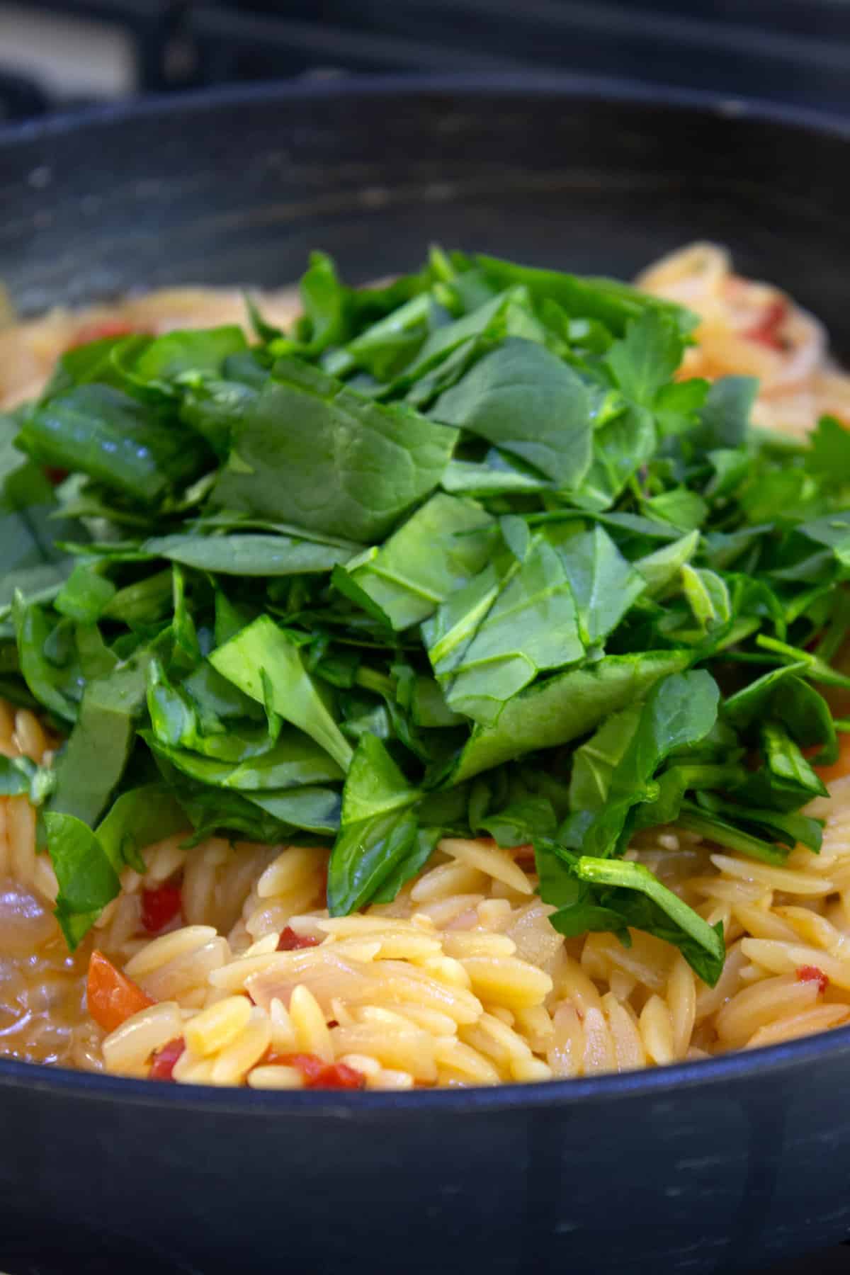 adding chopped spinach to orzo shrimp skillet