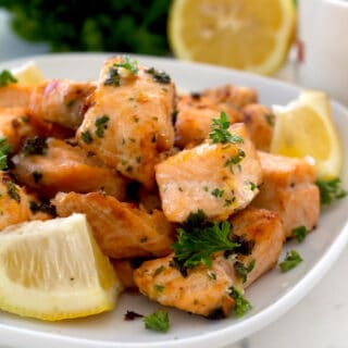 salmon bites on a white plate with lemon and parsley garnish