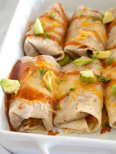 baked burritos in a pan with avocado and hot sauce garnish
