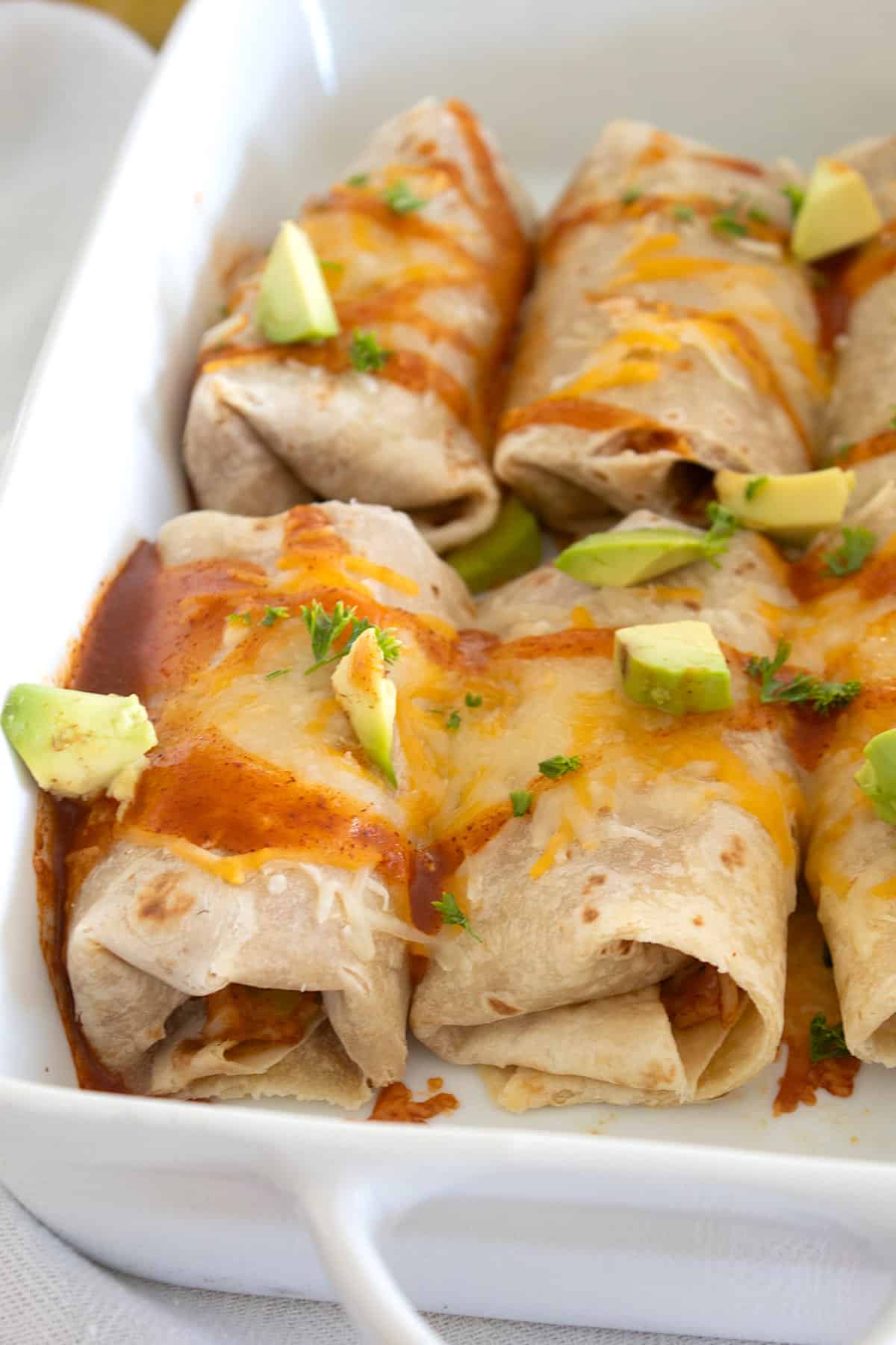 baked burritos in a pan with avocado and hot sauce garnish