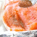 raw salmon filet with seasoning being sprinkled on it with a spoon