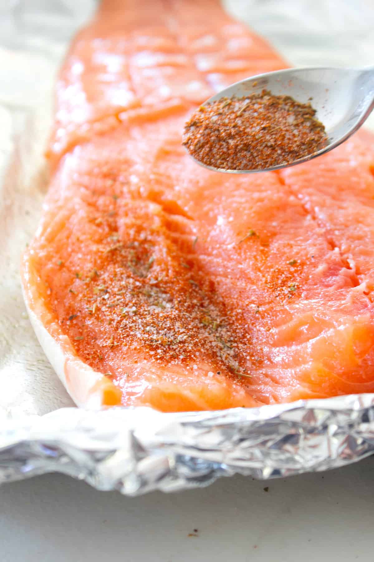 raw salmon filet with seasoning being sprinkled on it with a spoon