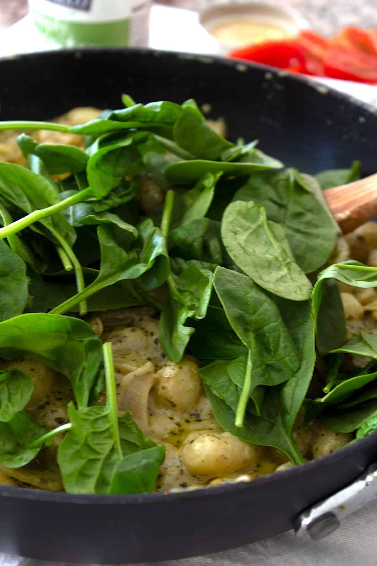 adding spinach to pesto gnocchi skillet